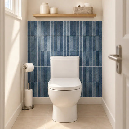 Mur des toilettes habillé de carrelage adhésif bleu indigo Oceana derrière la cuvette, étagère en bois au-dessus