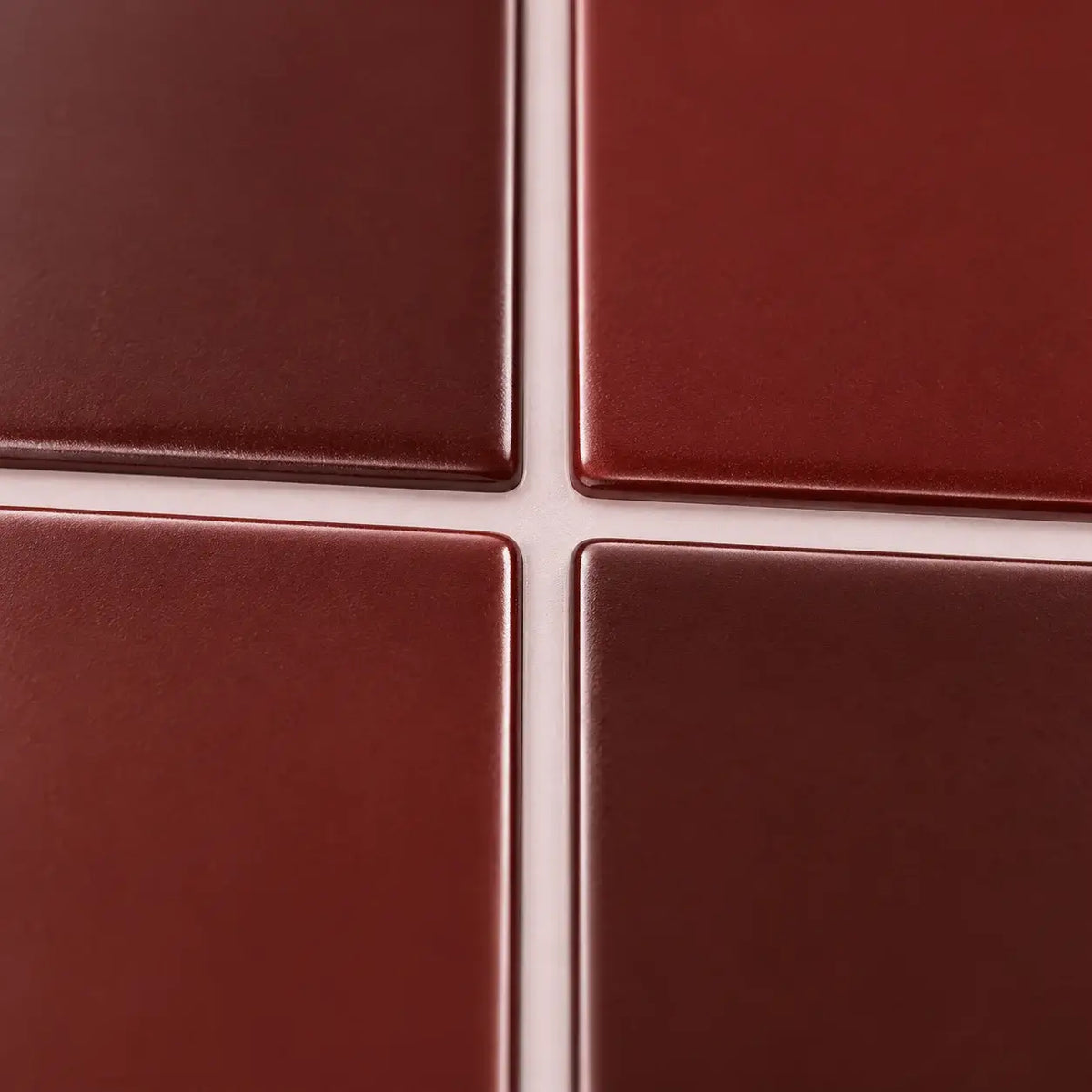 Gros plan sur les baguettes émaillées rouge bordeaux du carrelage adhésif et leurs joints blancs fins