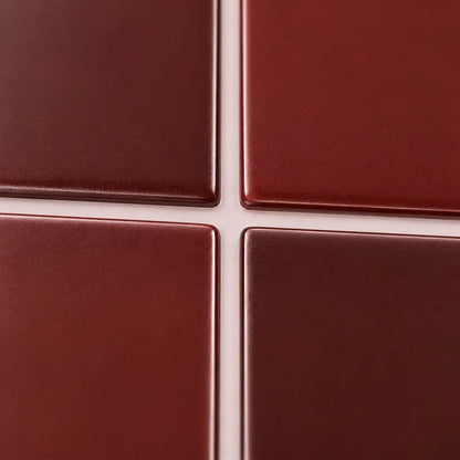 Gros plan sur les baguettes émaillées rouge bordeaux du carrelage adhésif et leurs joints blancs fins