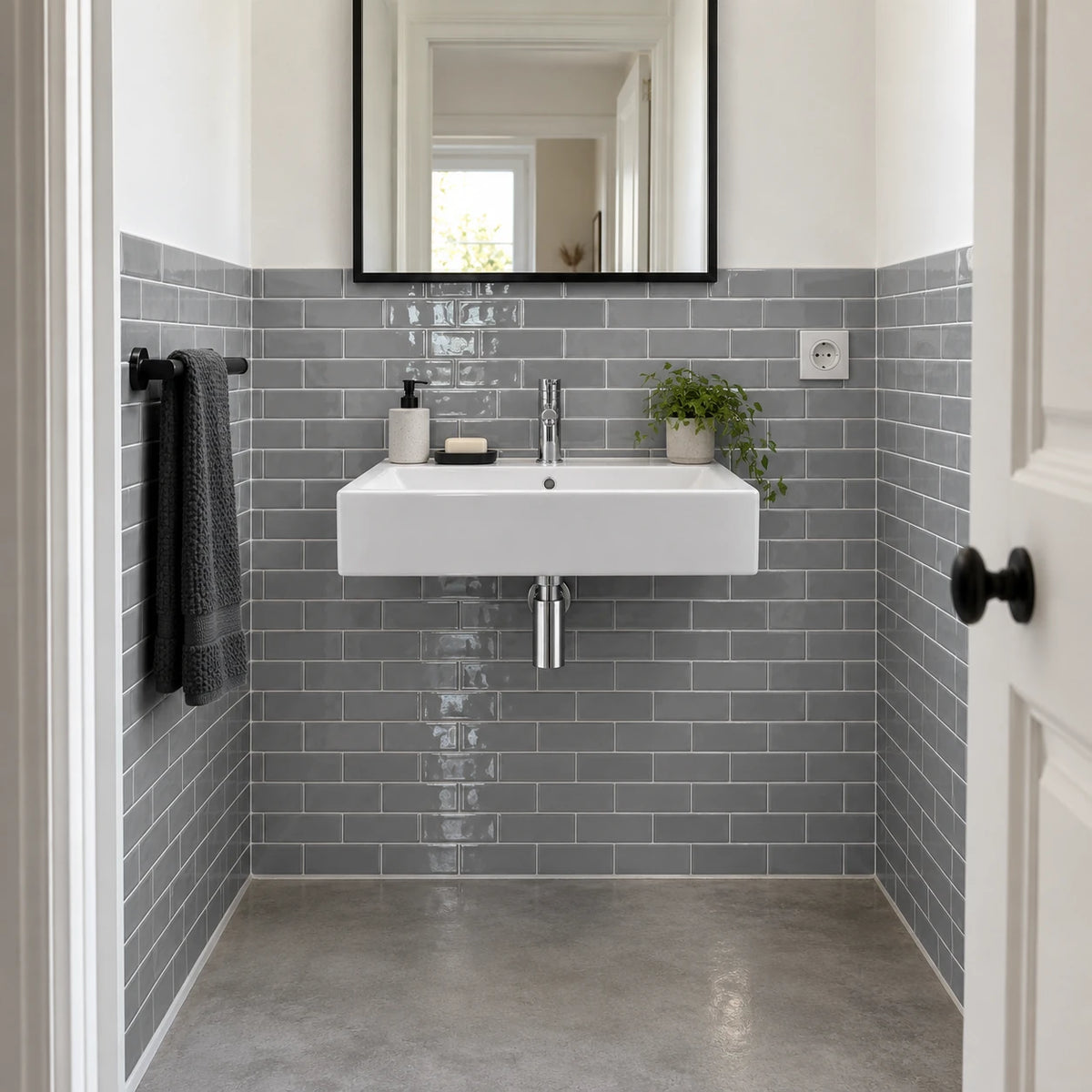 Salle de bain étroite avec carrelage adhésif métro gris à mi-hauteur, lavabo suspendu blanc et miroir à cadre noir
