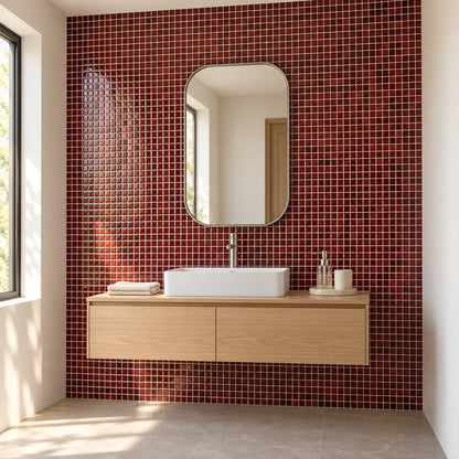 Mur de salle de bain en carrelage adhésif mosaïque bordeaux, meuble vasque suspendu en bois clair et miroir arrondi
