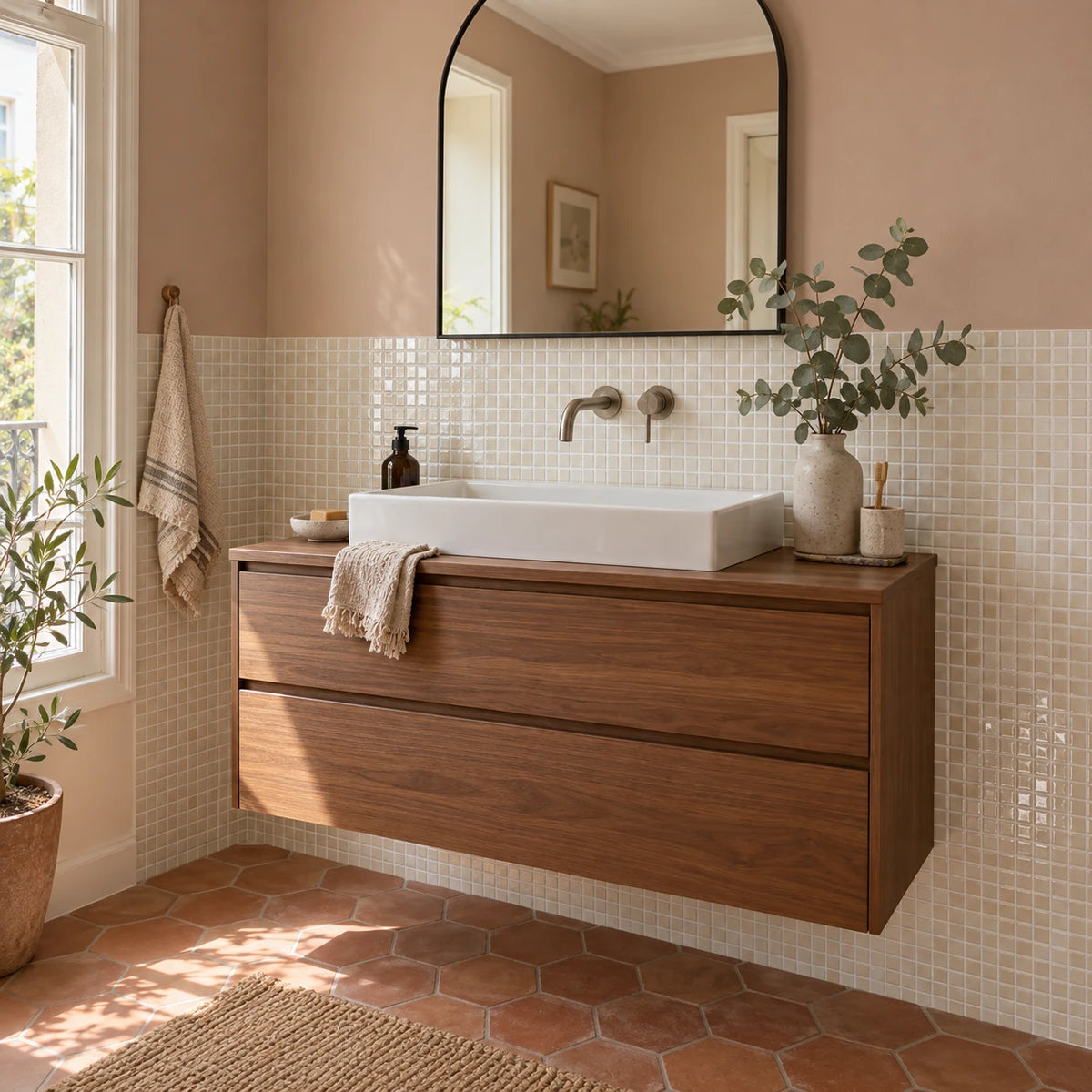 Salle de bain avec carrelage mural adhésif mosaïque ivoire, meuble vasque suspendu en noyer, miroir en arche et sol en tomettes